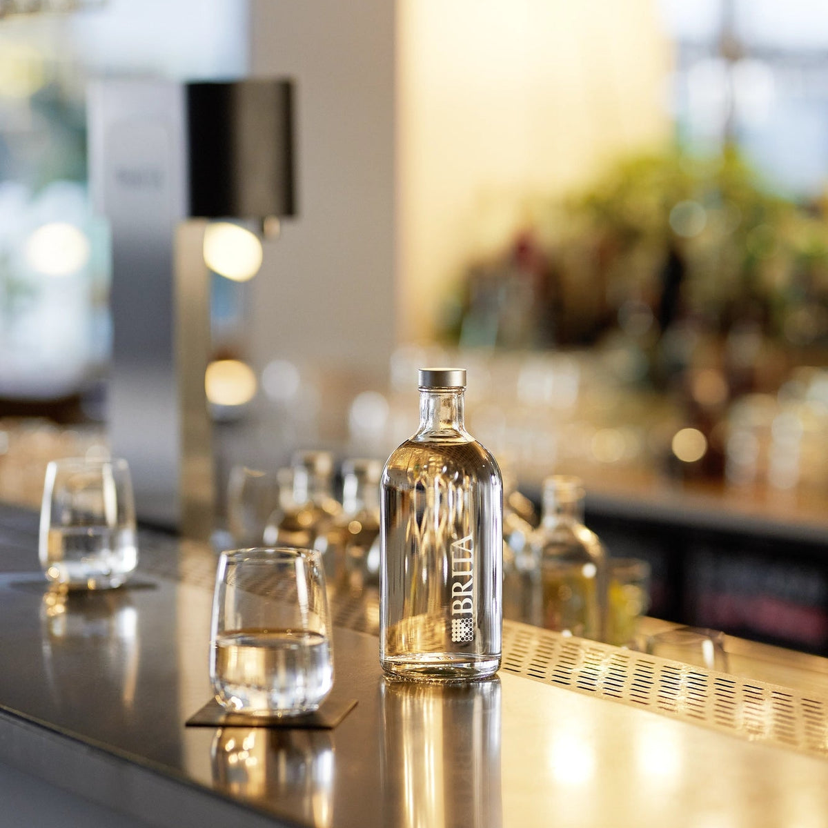 Een BRITA Lounge-fles op een bar, met glazen en een Fill T-Tap op de achtergrond.